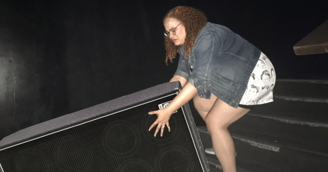 Woman Carrying Bass Cab up Flight of Stairs Starting to Regret Making a Point